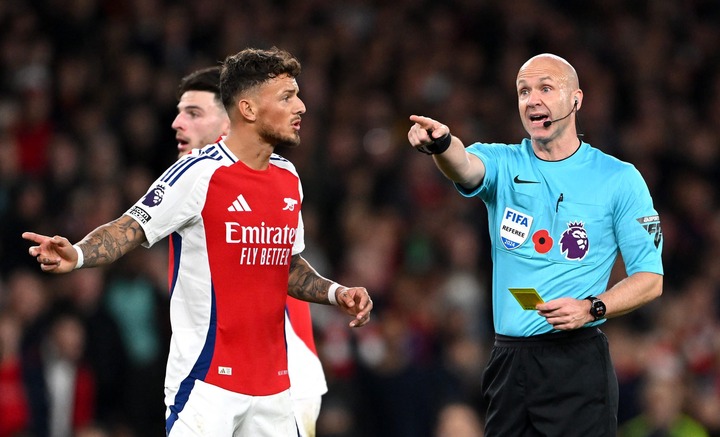 Referee Anthony Taylor shows a yellow card to Alexis Mac Allister of Liverpool (not pictured) as Ben White of Arsenal reacts during the Premier Lea...