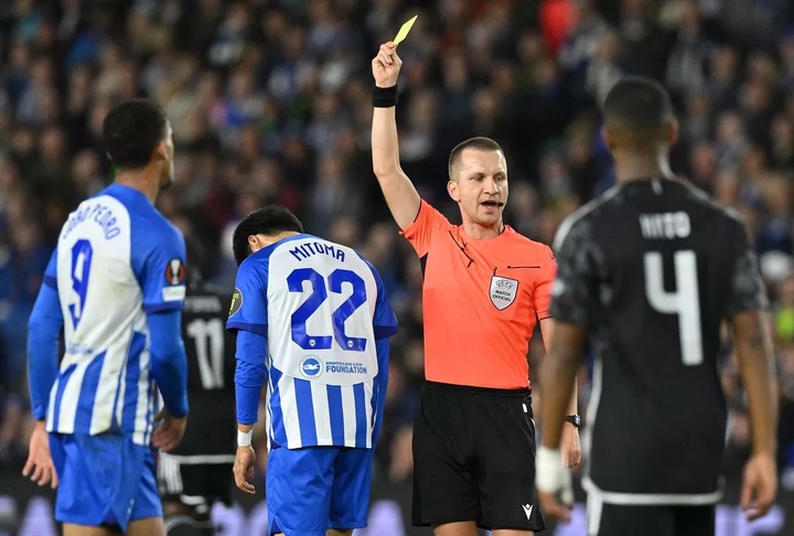 Polish Referee Bartosz Frankowski shows a yellow card to Brighton's Japanese midfielder #22 Kaoru Mitoma