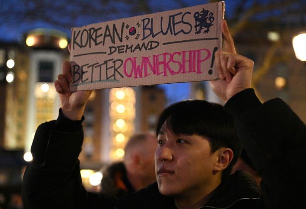 A fan of Chelsea is seen with a sign reading 'KOREAN BLUES DEMAND BETTER OWNERSHIP' 